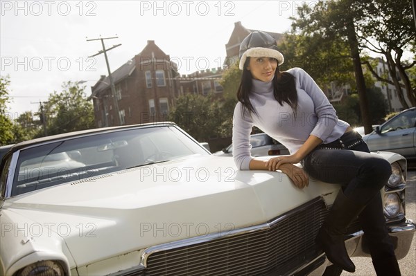 Hispanic woman leaning on hood of car