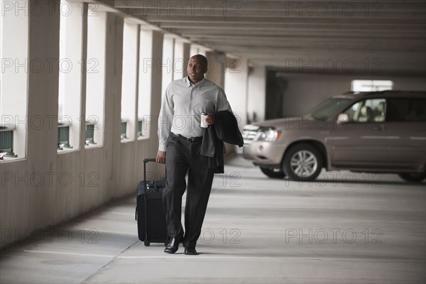 African businessman walking in parking garage with luggage