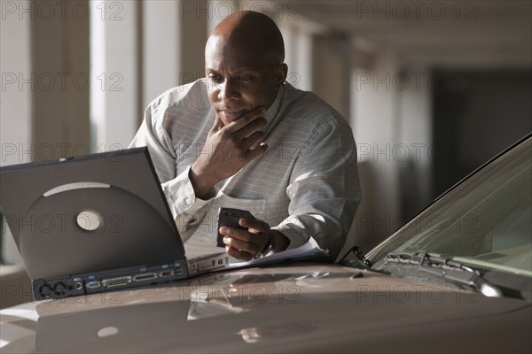 African businessman using laptop on car hood