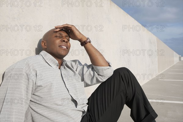 African businessman sitting on ground in parking lot