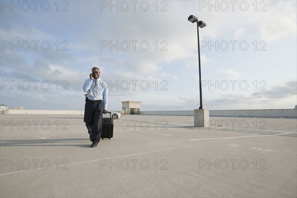 African businessman pulling luggage in parking lot
