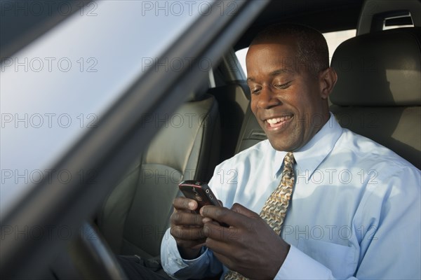 African businessman in car text messaging on cell phone