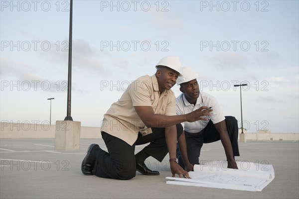 African businessmen looking at blueprints in parking lot