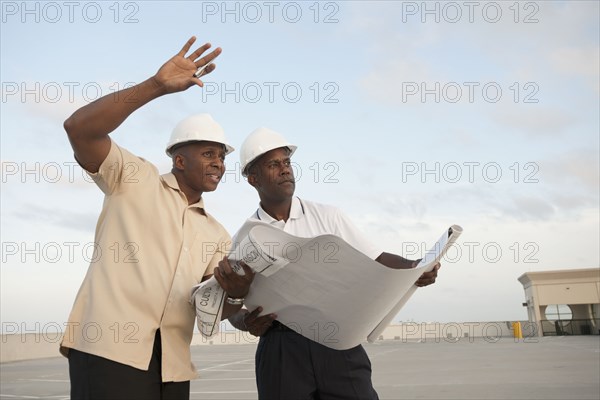 African businessmen looking at blueprints in parking lot