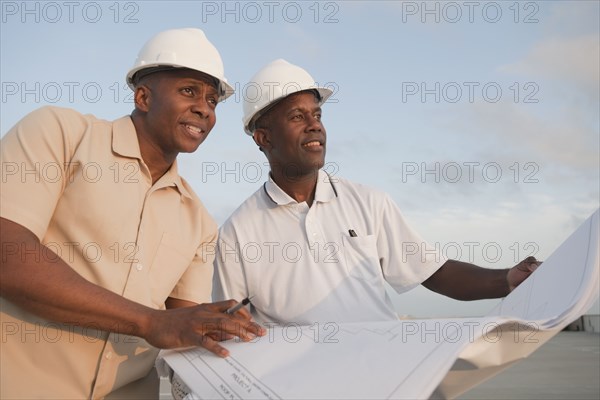 African businessmen looking at blueprints in parking lot