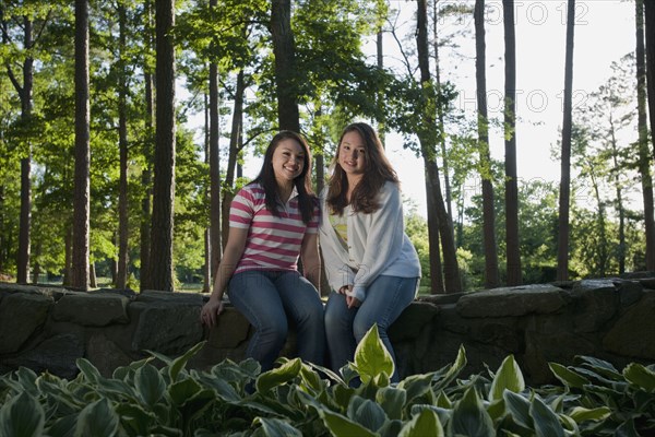 Mixed race friends sitting on stone wall