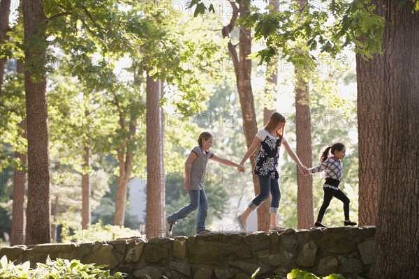 Friends holding hands and walking on stone wall