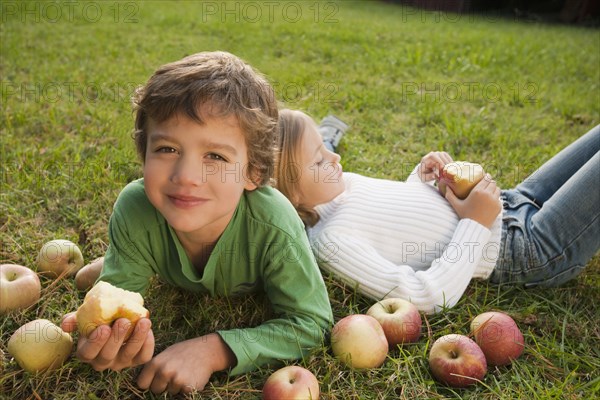 Mixed race brother and sister laying in grass with apples