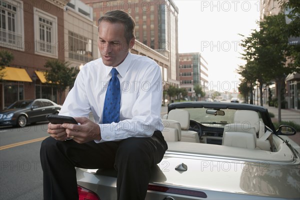 Caucasian businessman sitting on car text messaging on cell phone