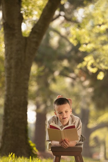 Caucasian boy reading book in yard