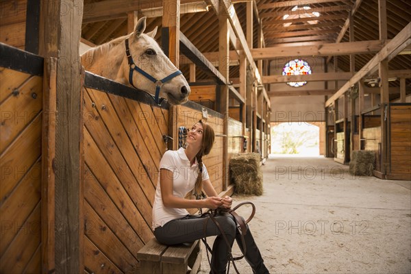 Caucasian girl sitting with horse in stable