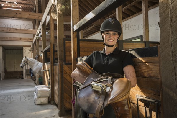 Caucasian girl carrying saddle in horse stable