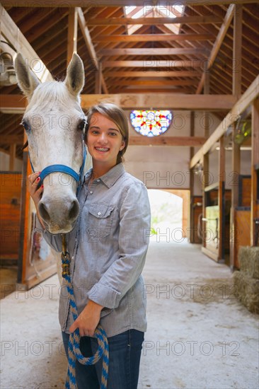 Caucasian girl smiling with horse in stable