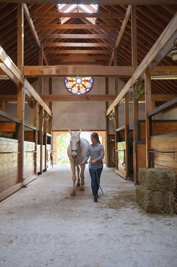 Caucasian girl walking horse in stable