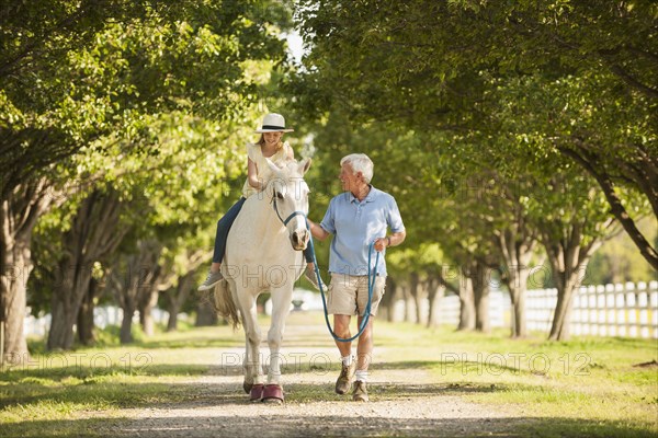 Caucasian man walking horse with granddaughter