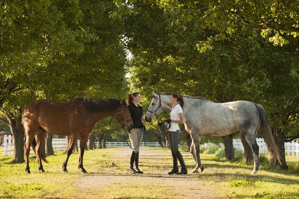 Caucasian girls walking horses on dirt path