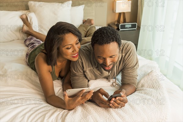 Couple using digital tablet and cell phone on bed