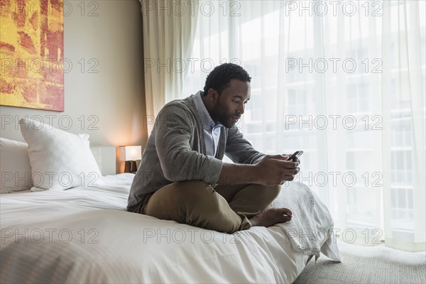 Black man using cell phone on bed