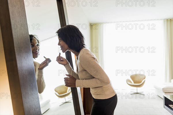 African American businesswoman applying lipstick in mirror