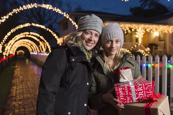 Caucasian mother and daughter holding Christmas gifts on sidewalk