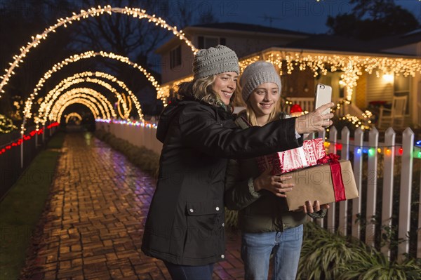 Caucasian mother and daughter holding Christmas gifts posing for selfie