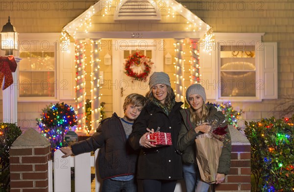 Caucasian family holding Christmas gifts on front stoop