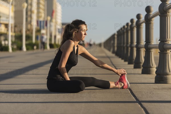 Caucasian teenage girl sitting on boardwalk stretching legs