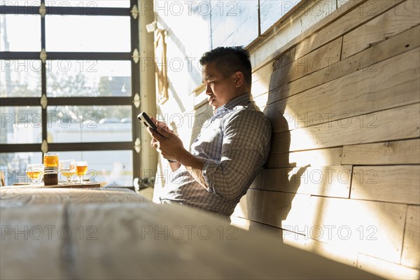 Asian man texting on cell phone in brew pub