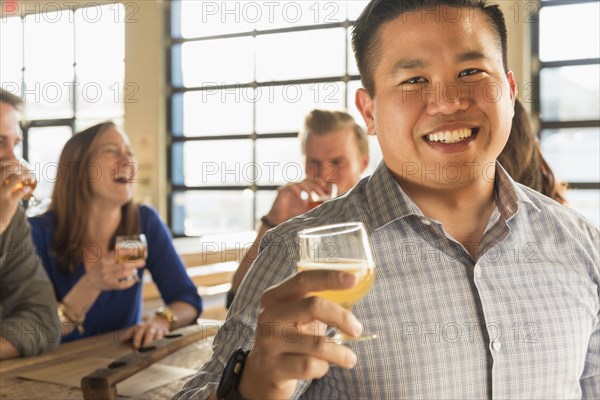 Portrait of smiling man drinking beer with friends in brew pub