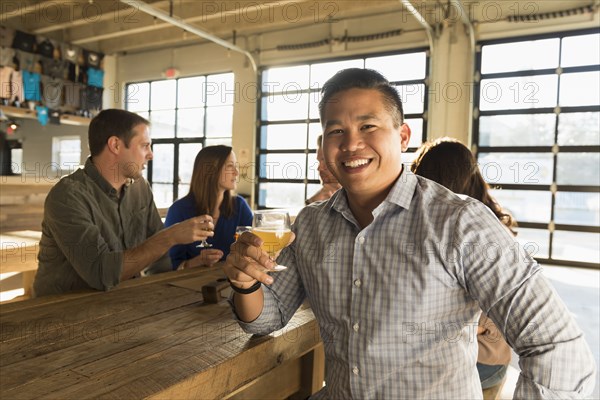 Portrait of smiling man drinking beer with friends in brew pub