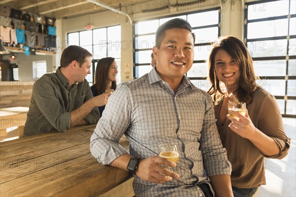 Portrait of smiling couple drinking beer with friends in brew pub