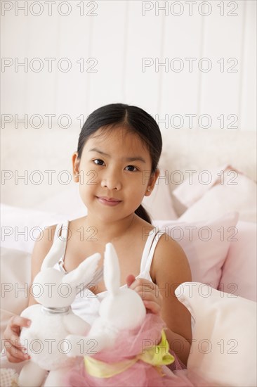 Asian girl on bed holding stuffed rabbits