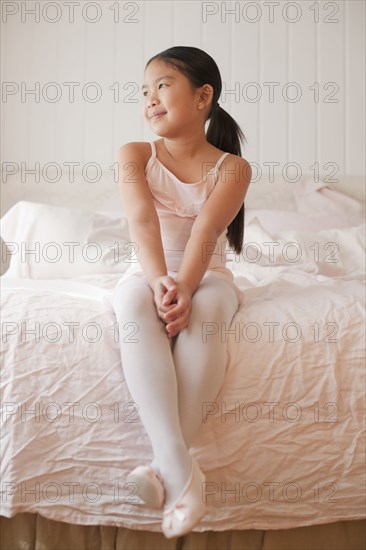 Asian girl in ballet costume sitting on bed