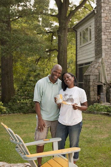 African American couple painting chair in backyard