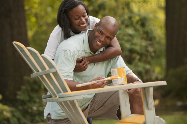 African American couple painting chair in backyard