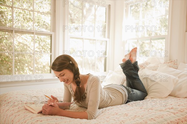 Mixed race girl laying in bed writing in journal
