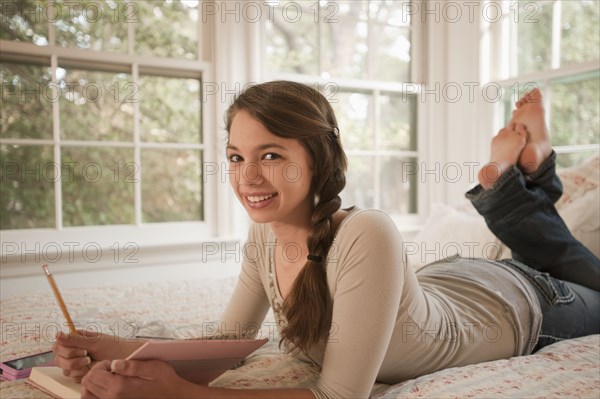 Mixed race girl laying in bed writing in journal