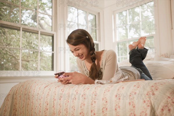 Mixed race girl laying in bed text messaging on cell phone