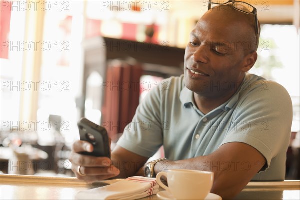 African American man in restaurant text messaging on cell phone