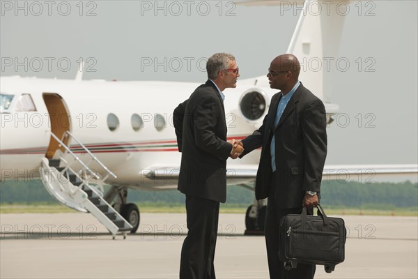 Businessmen shaking hands on airport tarmac