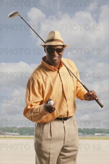 African American golfer with club and ball on tarmac