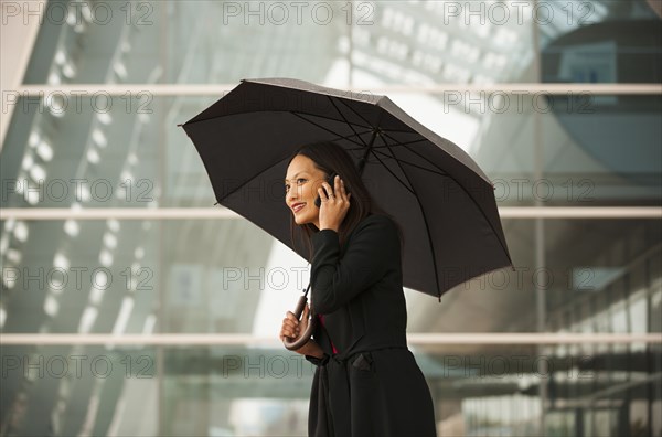 Asian businesswoman with umbrella talking on cell phone