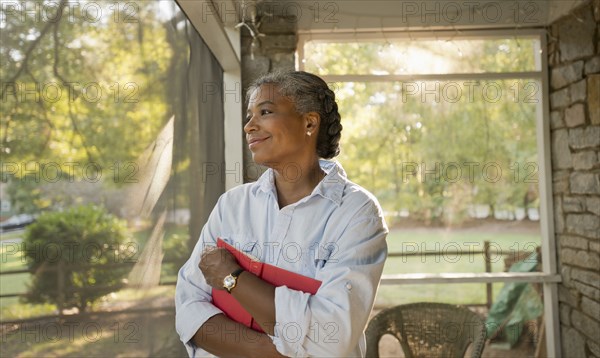 Mixed race woman holding book on porch