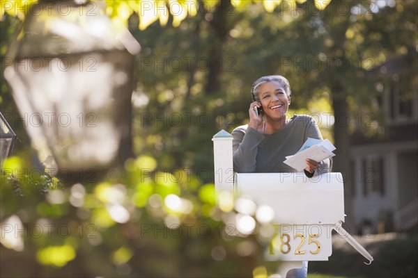 Mixed race woman holding mail and talking on cell phone