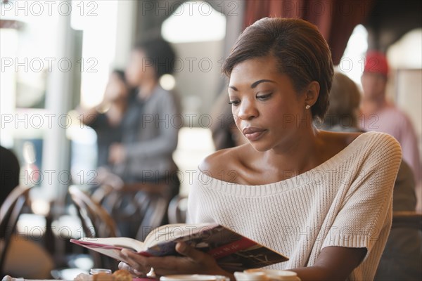 African American woman reading book in cafe