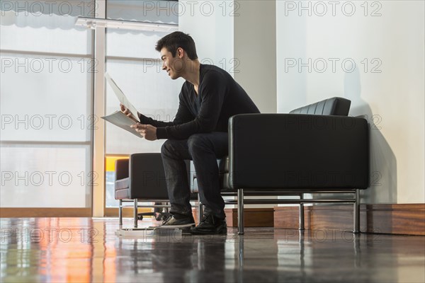 Mixed race businessman reading papers in office lobby