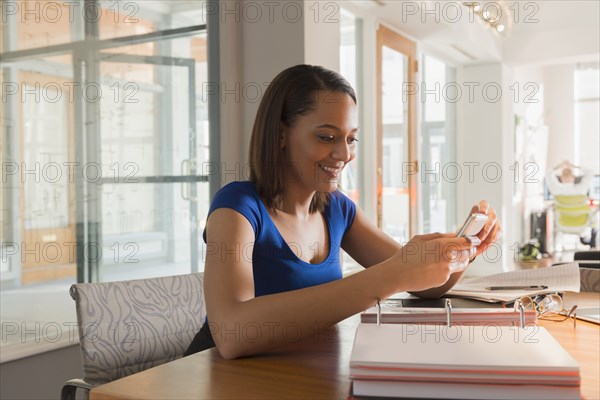 Mixed race businesswoman taking cell phone pictures at desk