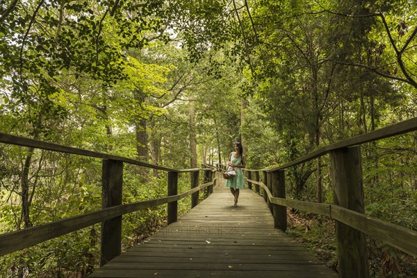 Hispanic woman walking on wooden footbridge in forest
