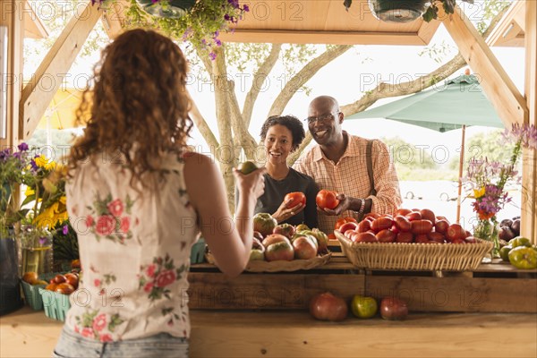 Vendor showing produce to couple at farmers market