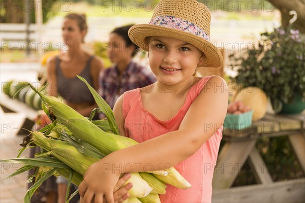 Mixed race girl carrying corn stalks at farmers market